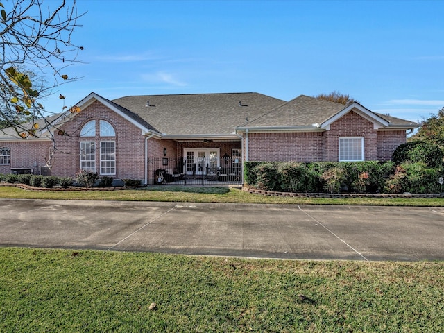 ranch-style house featuring a shingled roof, a front yard, and brick siding