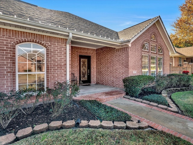 doorway to property with a shingled roof and brick siding