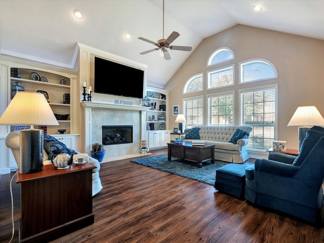 living room with ceiling fan, high vaulted ceiling, wood finished floors, built in features, and a tiled fireplace