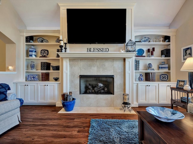 living room featuring built in shelves, dark wood-style flooring, and a tiled fireplace