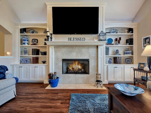 living room featuring dark wood-type flooring, a tile fireplace, and built in shelves