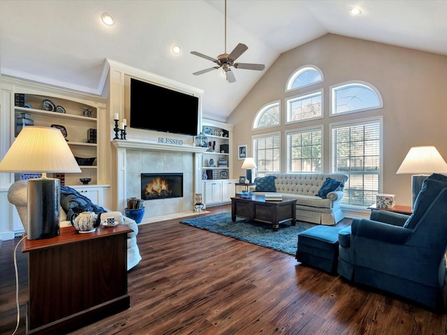 living room with built in shelves, a tiled fireplace, ceiling fan, wood finished floors, and high vaulted ceiling