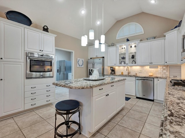 kitchen with light tile patterned floors, stainless steel appliances, a kitchen island, white cabinets, and tasteful backsplash