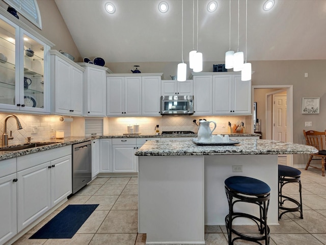 kitchen featuring white cabinets, lofted ceiling, appliances with stainless steel finishes, a center island, and a sink