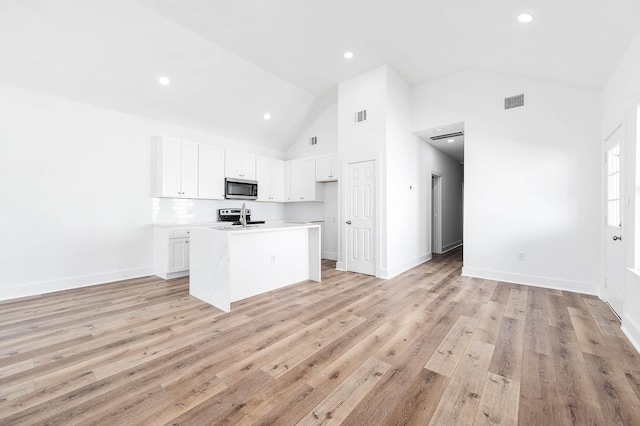 kitchen featuring white cabinets, an island with sink, stainless steel microwave, light countertops, and a sink