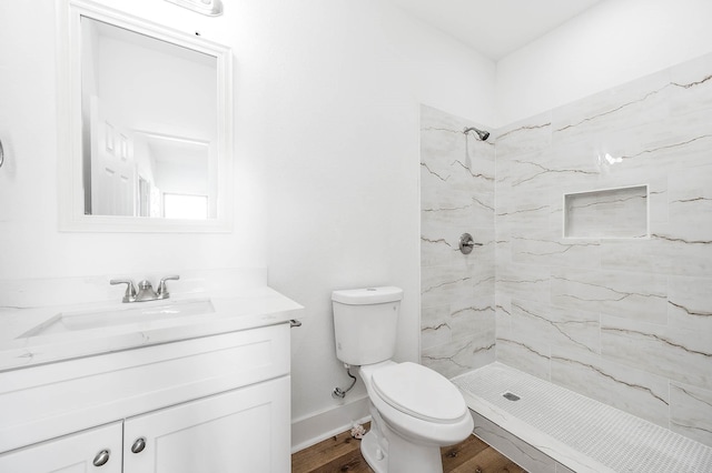 bathroom featuring toilet, a tile shower, vanity, wood finished floors, and baseboards