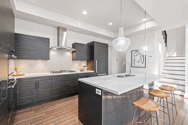 kitchen with stainless steel gas cooktop, a sink, wall chimney range hood, modern cabinets, and a raised ceiling