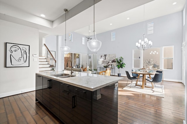 kitchen with dark wood-style flooring, a sink, a towering ceiling, and an island with sink