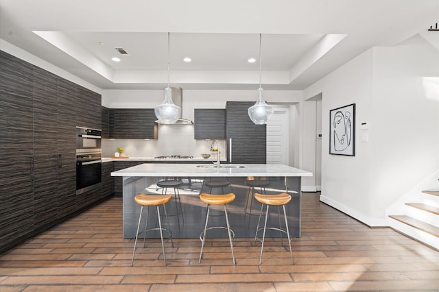 kitchen with a tray ceiling, light countertops, wall chimney range hood, and modern cabinets