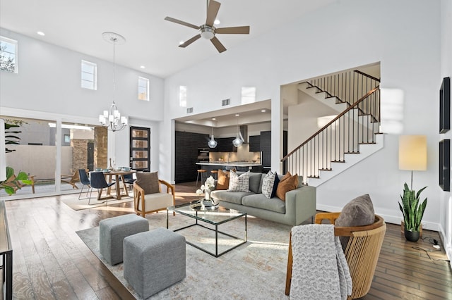 living room with hardwood / wood-style flooring, ceiling fan with notable chandelier, a towering ceiling, baseboards, and stairway