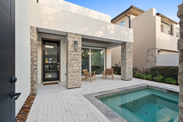 back of property featuring stone siding, an in ground hot tub, and stucco siding