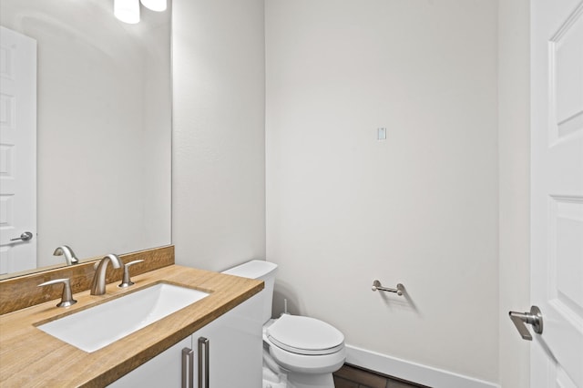 half bath with vanity, toilet, and baseboards