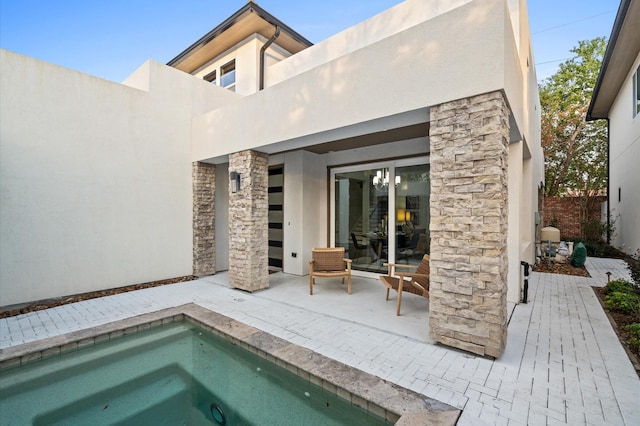 rear view of property with stone siding, a patio area, an in ground hot tub, and stucco siding