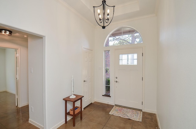 tiled entrance foyer with a raised ceiling, crown molding, baseboards, and an inviting chandelier