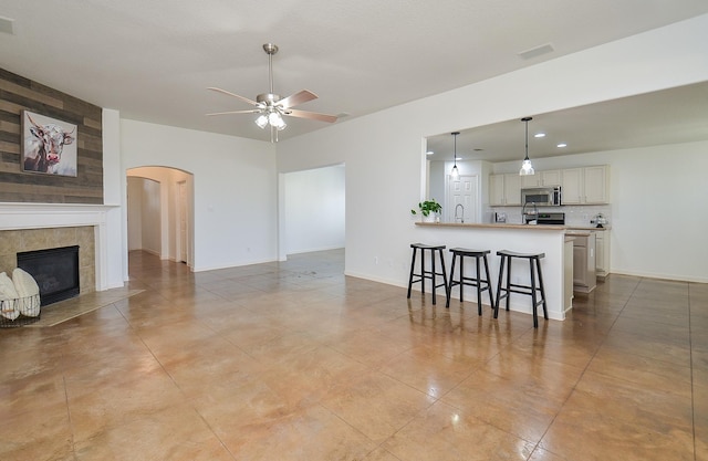 living room featuring baseboards, visible vents, arched walkways, a tiled fireplace, and ceiling fan