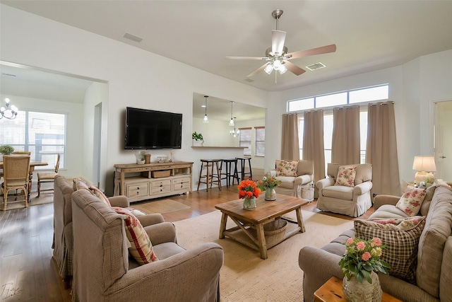 living room featuring ceiling fan with notable chandelier, visible vents, and wood finished floors