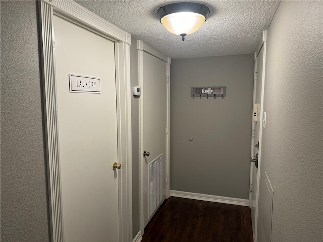 hallway featuring dark wood-style floors, visible vents, a textured ceiling, and baseboards