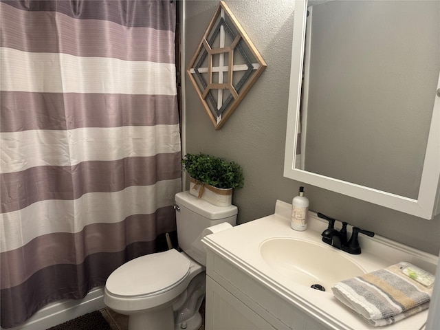 bathroom featuring curtained shower, a textured wall, vanity, and toilet