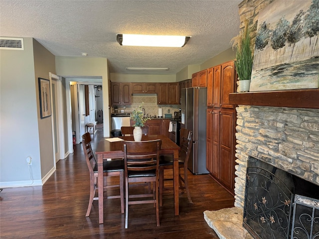 dining area with baseboards, visible vents, dark wood-style flooring, a textured ceiling, and a stone fireplace