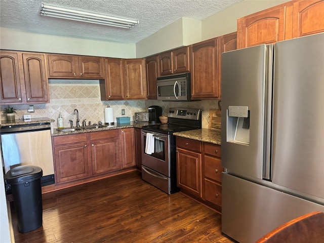 kitchen featuring stainless steel appliances, a sink, decorative backsplash, dark stone countertops, and dark wood finished floors