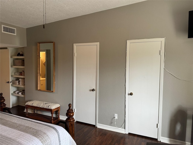 bedroom with baseboards, a textured ceiling, visible vents, and wood finished floors