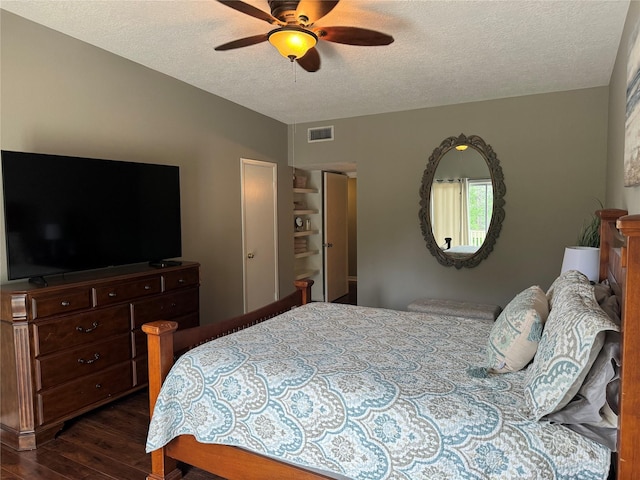 bedroom with a textured ceiling, dark wood finished floors, visible vents, and a ceiling fan