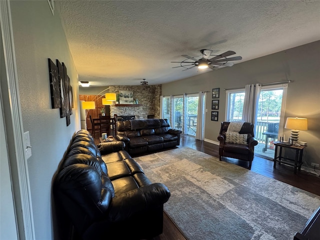 living area featuring a textured ceiling, a ceiling fan, wood finished floors, and a stone fireplace