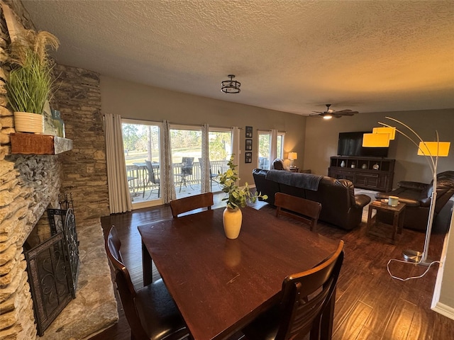 dining space with a textured ceiling, ceiling fan, a stone fireplace, and wood finished floors