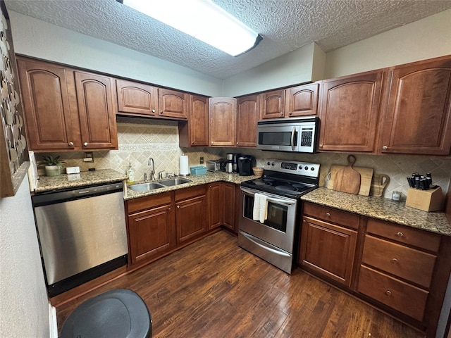 kitchen with dark wood-type flooring, a sink, light stone countertops, stainless steel appliances, and backsplash