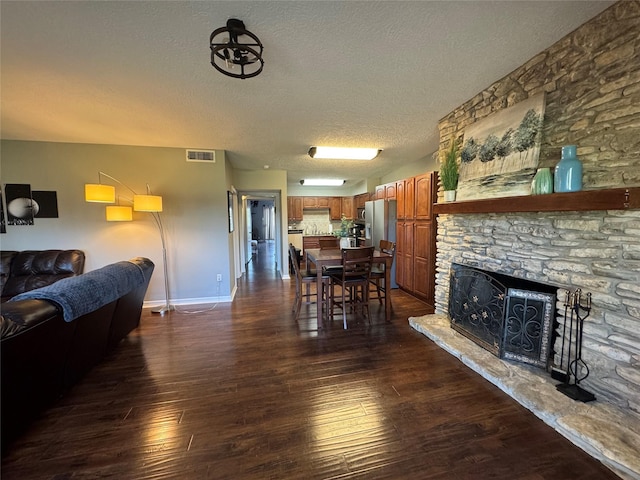 dining space with dark wood-style floors, a fireplace, visible vents, a textured ceiling, and baseboards