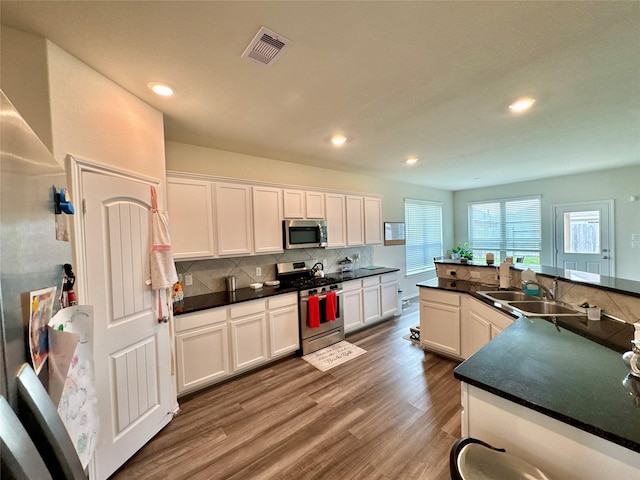 kitchen featuring stainless steel appliances, dark countertops, visible vents, a sink, and wood finished floors