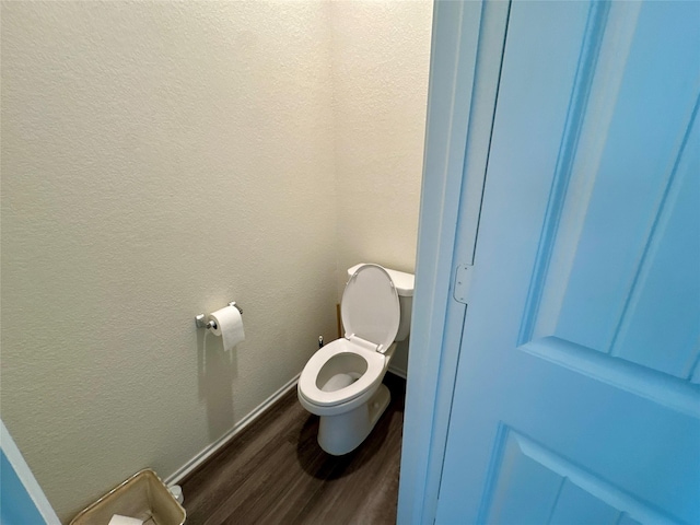 bathroom featuring toilet, baseboards, wood finished floors, and a textured wall