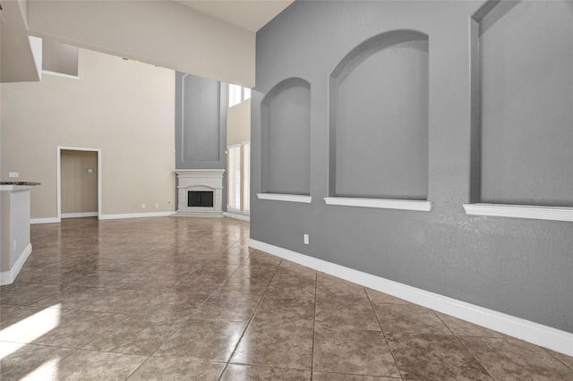 unfurnished living room featuring a towering ceiling, baseboards, a fireplace with raised hearth, and tile patterned floors