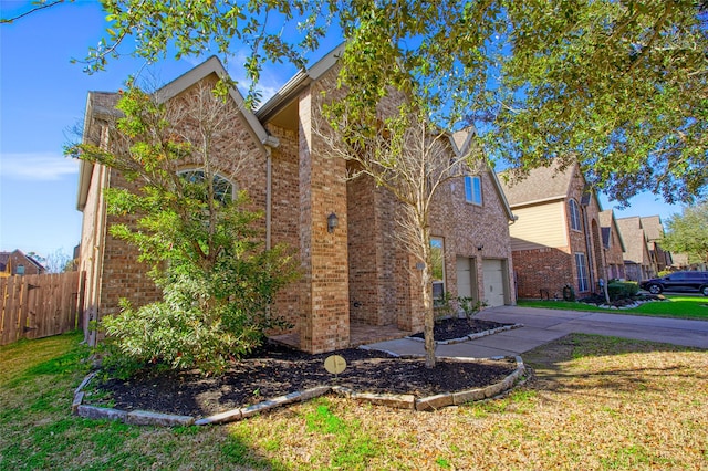 view of side of home with a yard, brick siding, driveway, and fence