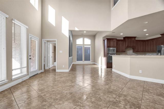 kitchen featuring baseboards, appliances with stainless steel finishes, open floor plan, backsplash, and light tile patterned flooring