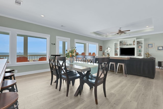 dining room featuring light wood-style floors, a raised ceiling, visible vents, and baseboards