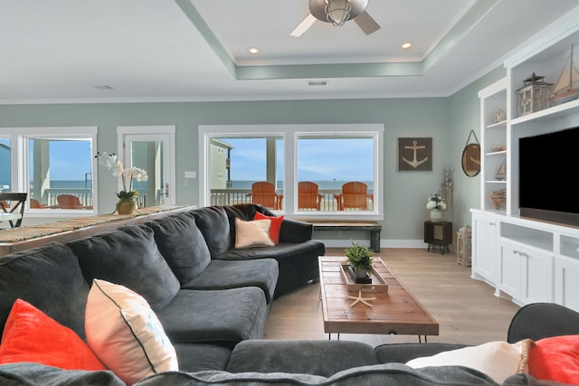 living area featuring visible vents, baseboards, ornamental molding, a tray ceiling, and light wood-type flooring