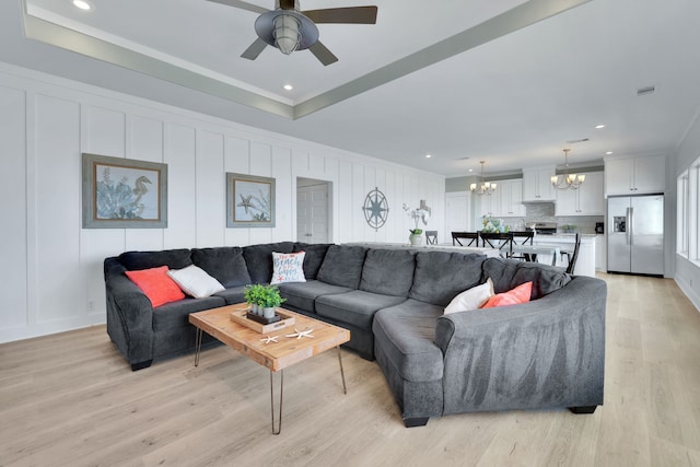 living area featuring crown molding, ceiling fan with notable chandelier, light wood-type flooring, and a decorative wall