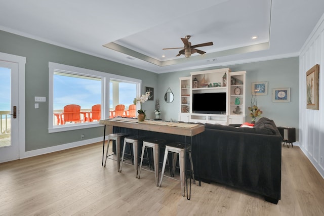 living room with ornamental molding, light wood-type flooring, a raised ceiling, and baseboards