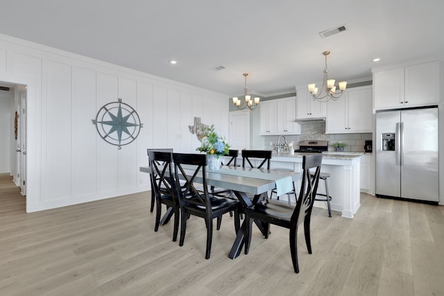 dining room featuring a chandelier, light wood-style floors, visible vents, and a decorative wall