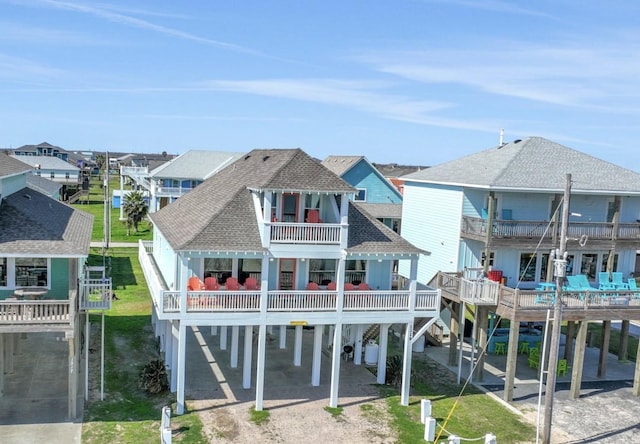 back of house featuring driveway, a balcony, roof with shingles, a yard, and a carport