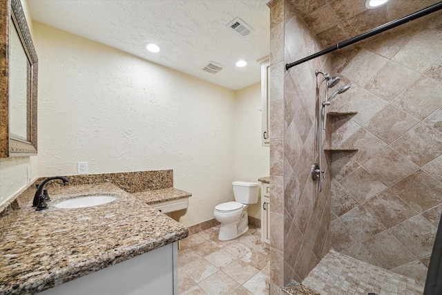 bathroom with a tile shower, visible vents, toilet, and vanity