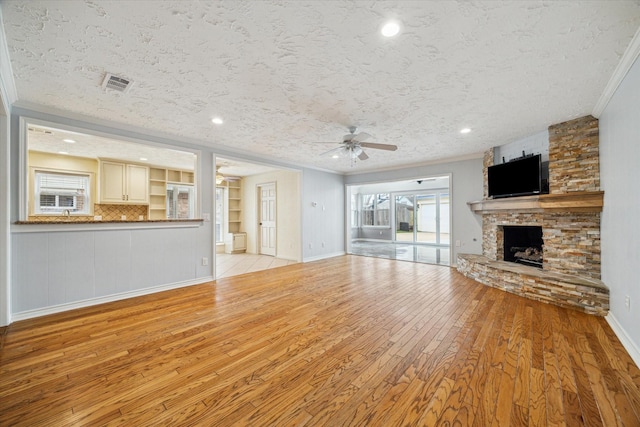 unfurnished living room featuring light wood finished floors, ornamental molding, a textured ceiling, and a fireplace