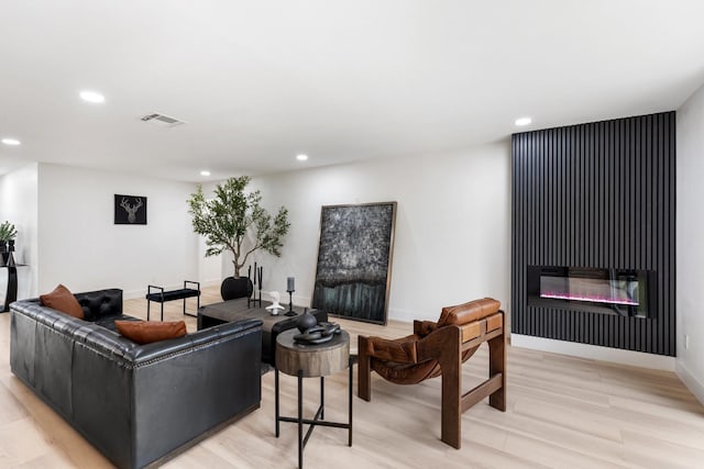 living area featuring light wood-type flooring, a glass covered fireplace, visible vents, and recessed lighting