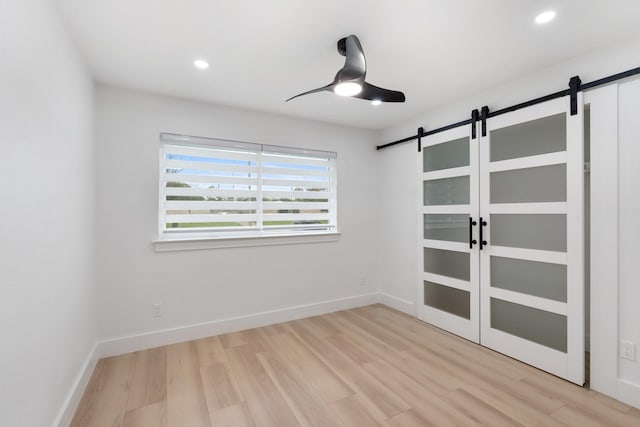 empty room with light wood-style floors, a barn door, baseboards, and recessed lighting