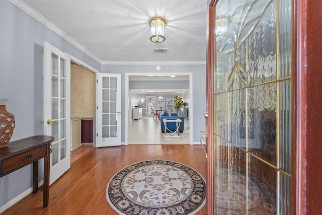 foyer entrance featuring a textured ceiling, wood finished floors, visible vents, ornamental molding, and french doors