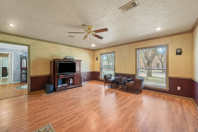 interior space featuring visible vents, a wainscoted wall, wood finished floors, crown molding, and a textured ceiling