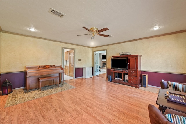 living room with light wood finished floors, ceiling fan, visible vents, and crown molding