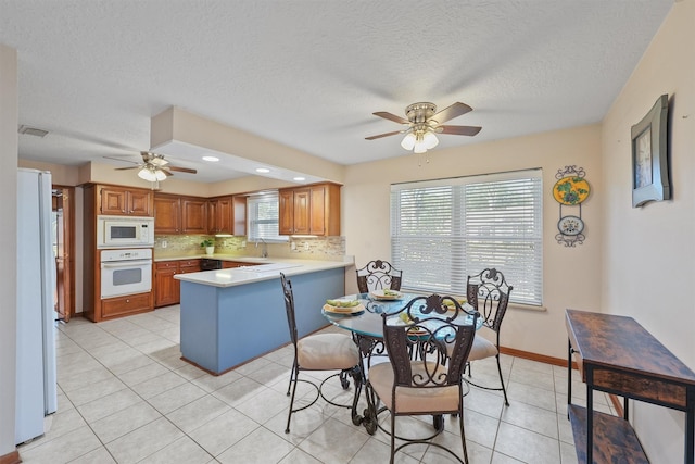 kitchen featuring brown cabinets, light tile patterned floors, light countertops, decorative backsplash, and white appliances