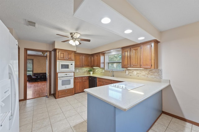 kitchen with brown cabinets, white appliances, light countertops, and a peninsula